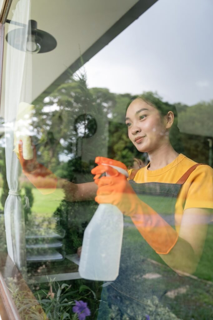 Young Asian housewife cleaning window glass with rags and detergent spray, cleaning house on the